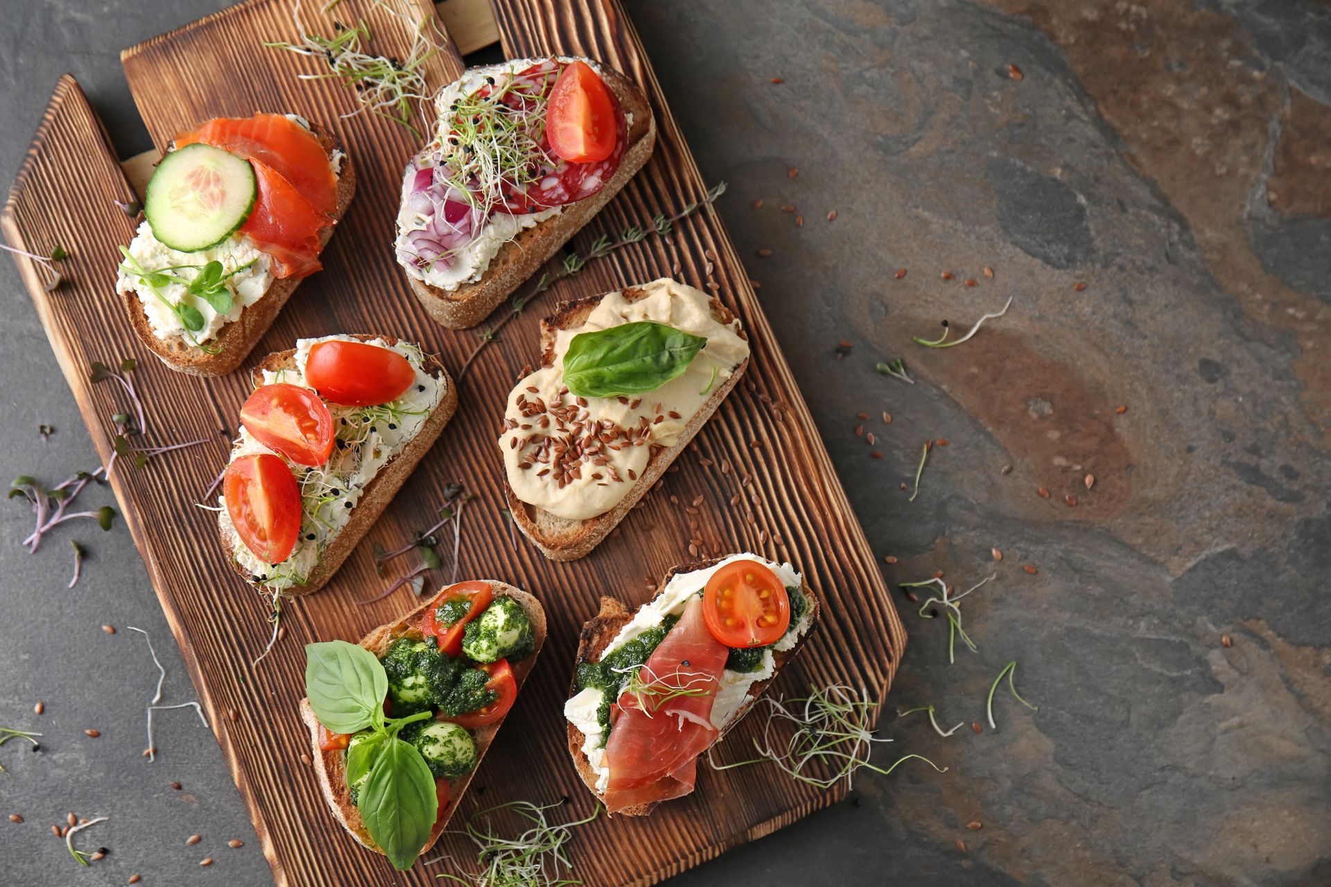 Assortiment de tartines sur une planche en bois avec légumes, herbes et saumon fumé.