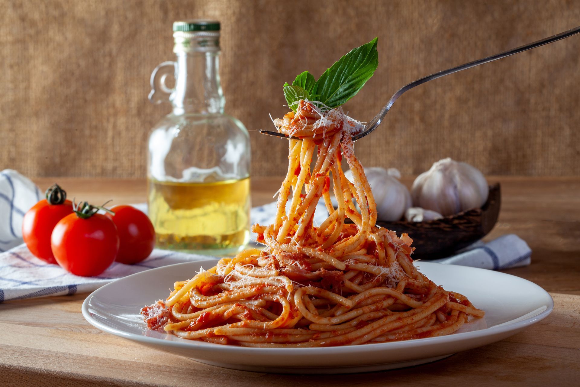 Spaghettis enroulés sur une assiette avec sauce tomate, basilic, tomates, ail et huile d'olive en arrière-plan.