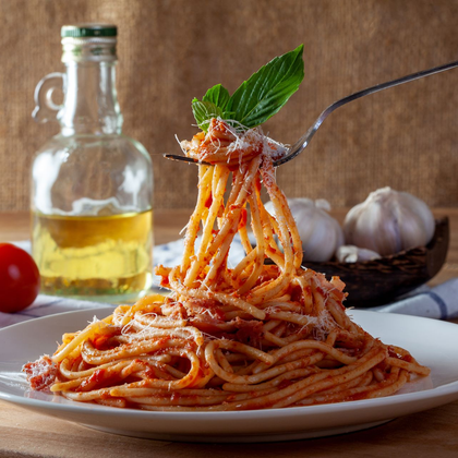 Assiette de spaghettis à la sauce tomate relevés sur une fourchette, avec de l'huile d'olive, des tomates et de l'ail en arrière-plan.