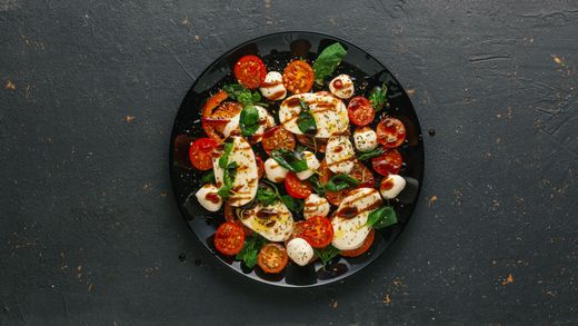 Vue de dessus d'une salade colorée composée de tomates, de mozzarella et de verdure, servie sur une assiette sombre.