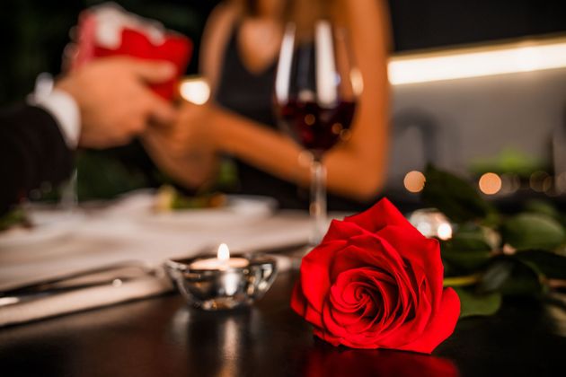 Une rose rouge sur une table sombre lors d'un dîner romantique aux chandelles et aux verres à vin embués.