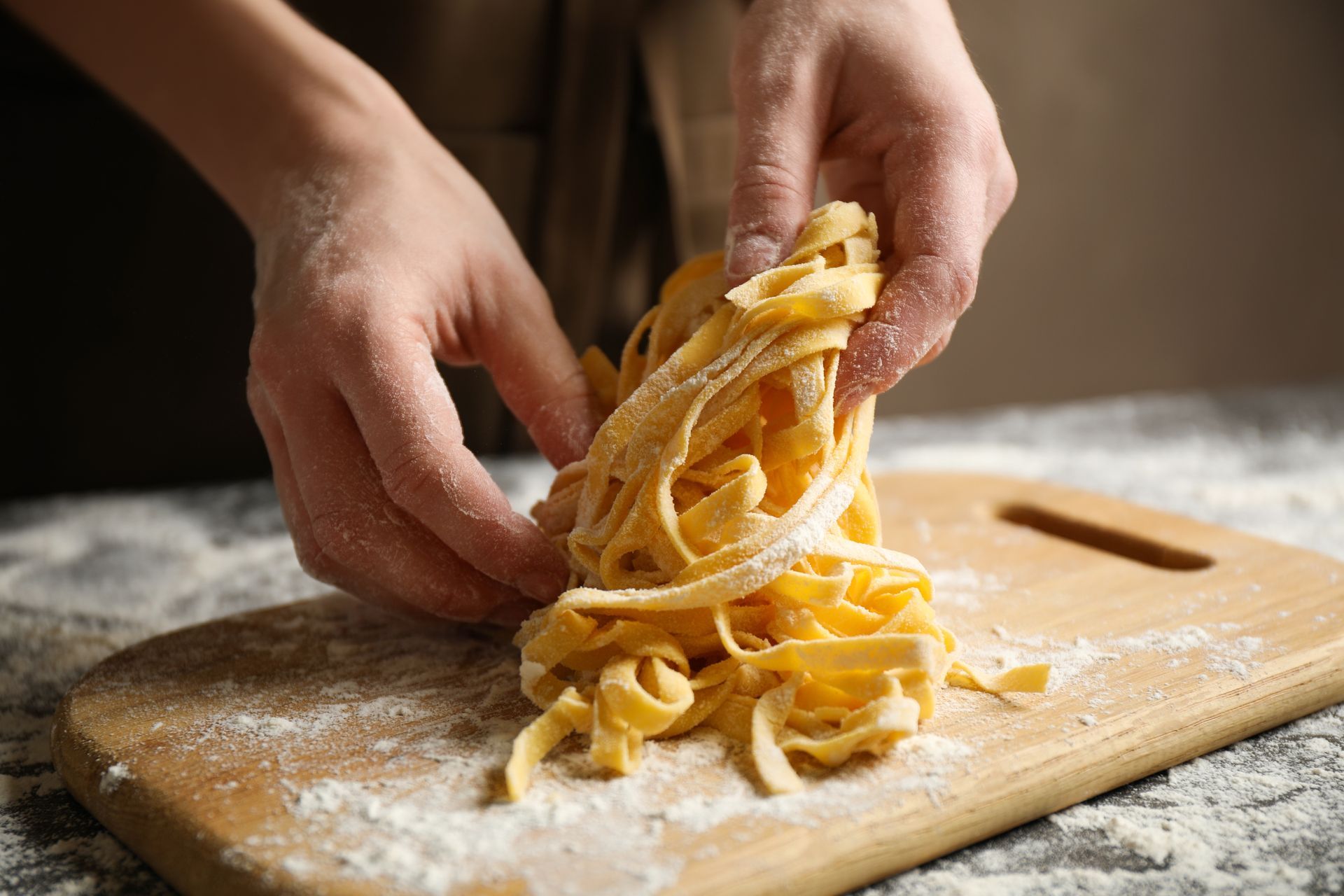 Des mains qui font tournoyer des pâtes fraîches sur une planche en bois farinée.