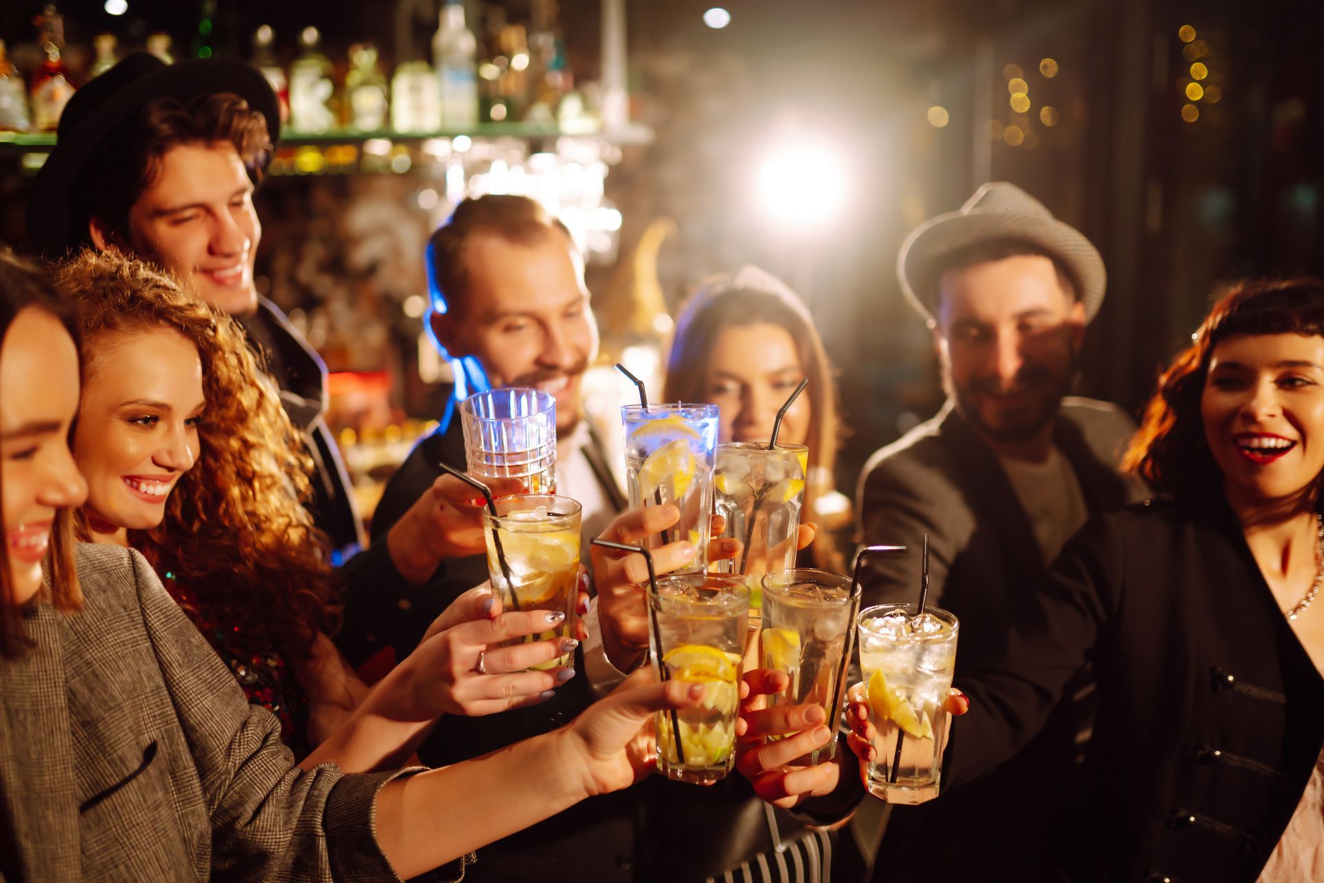 Des amis trinquent avec des cocktails dans un bar à l'éclairage chaleureux, souriant et discutant lors d'une fête.