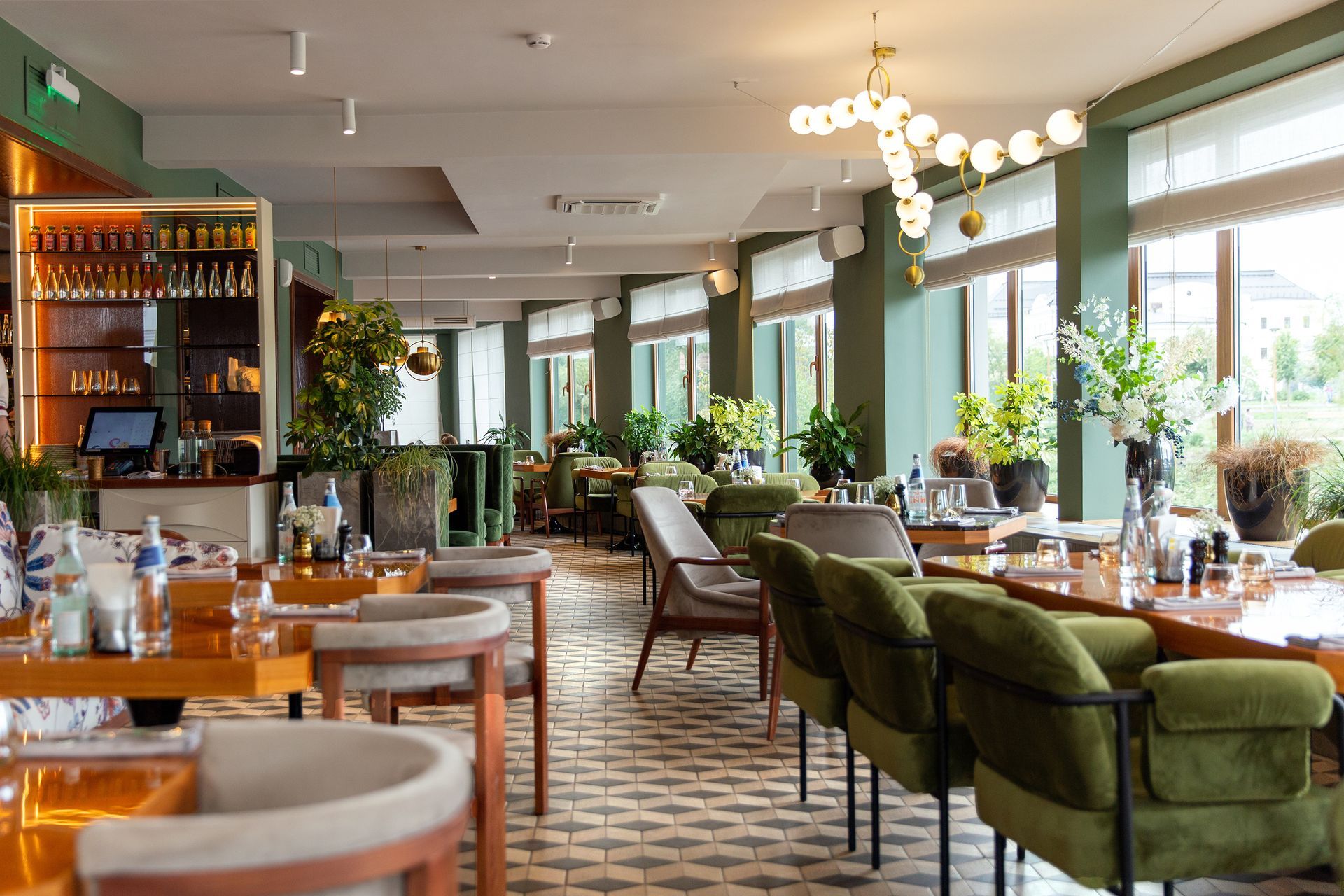 Intérieur de restaurant élégant avec chaises en velours vert, tables dressées, lustres et grandes fenêtres.