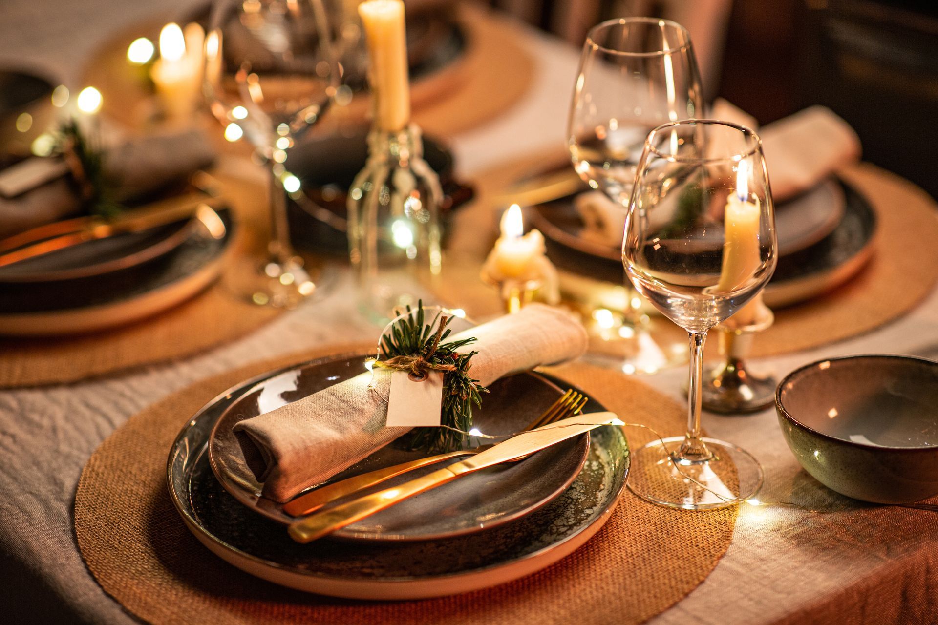 Élégante table à manger éclairée aux chandelles avec assiettes dorées, verres à vin et serviettes pliées, dressée pour un repas formel.