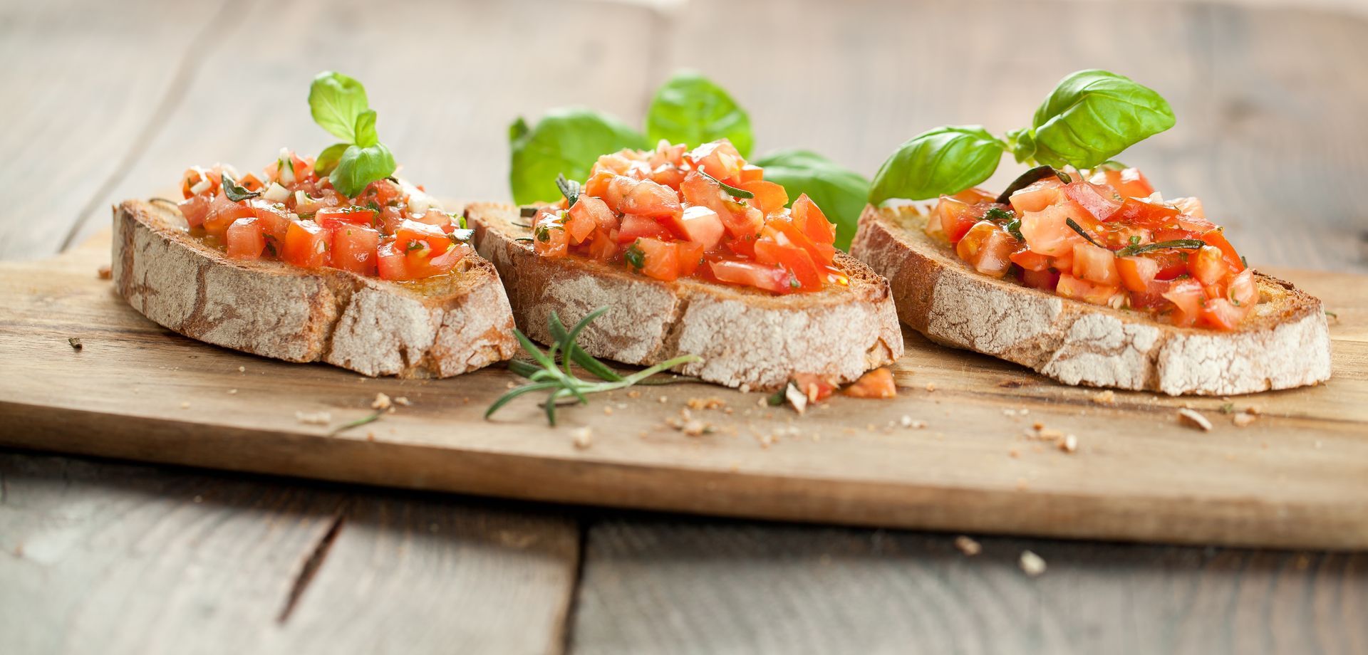 Trois tranches de bruschetta garnies de dés de tomates et de basilic, présentées sur une planche en bois.