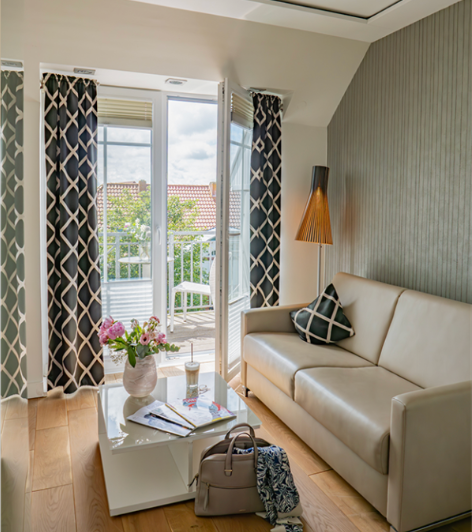 Sandstrand mit hohem Gras im Vordergrund, Meer und untergehende Sonne im Hintergrund.