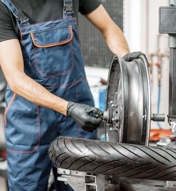 Mecánico con mono azul cambiando un neumático de motocicleta, con guantes negros, en un taller.