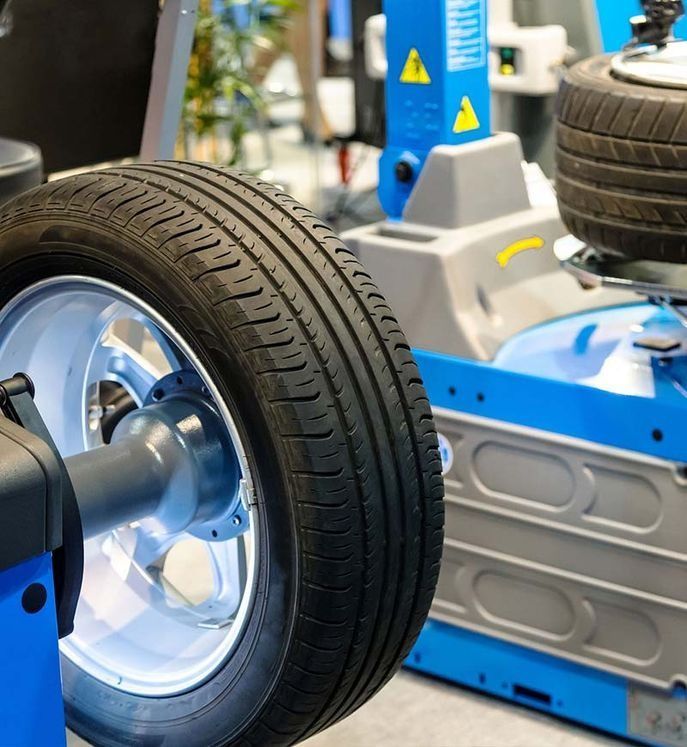 Neumático de una rueda equilibrado por una máquina azul y gris en un garaje.