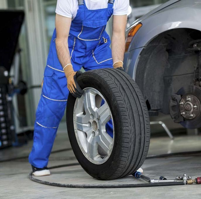 Mecánico con mono azul, cambiando un neumático de coche en un garaje.