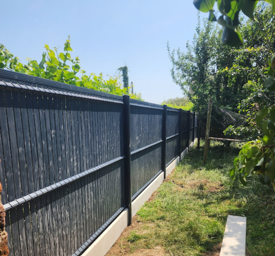 Clôture noire pour préserver l'intimité d'une cour gazonnée avec des arbres et un ciel d'un bleu éclatant.