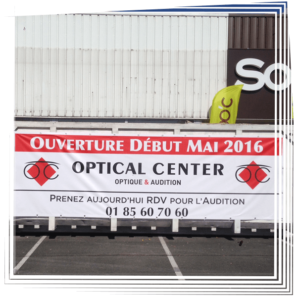 Bannière en français sur la façade du centre d'optique annonçant l'ouverture en février 2016 et la prise de rendez-vous en audiologie.