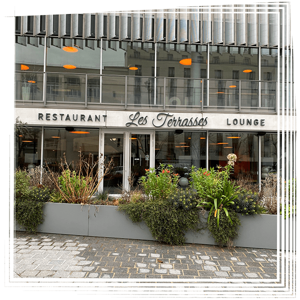 Vue au niveau de la rue du restaurant Les Terrasses avec son enseigne lounge et ses jardinières extérieures.