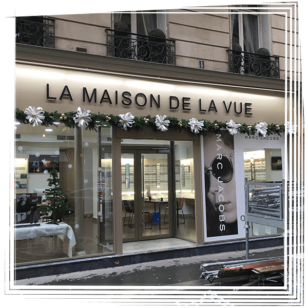 Façade de La Maison de la Vue avec portes vitrées, guirlande de fleurs blanches et enseigne de lunettes