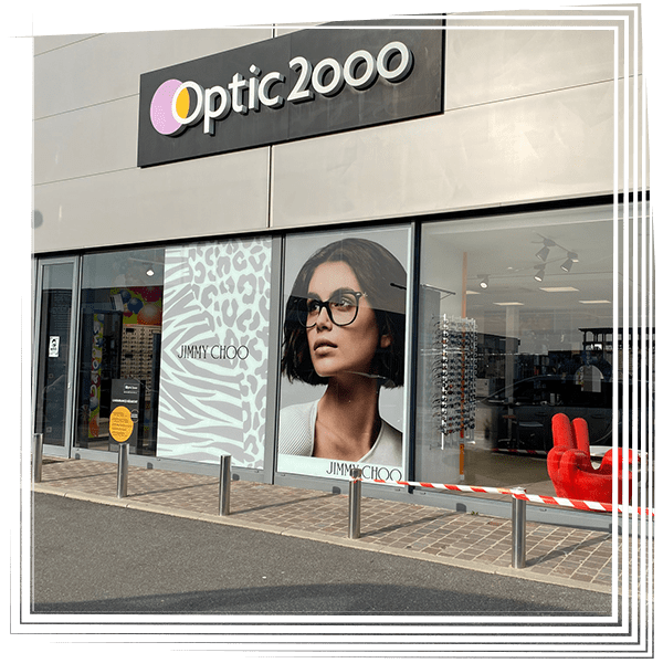 Façade du magasin Optic 2000 avec de grandes publicités pour lunettes et une chaise rouge exposée derrière des vitrines.