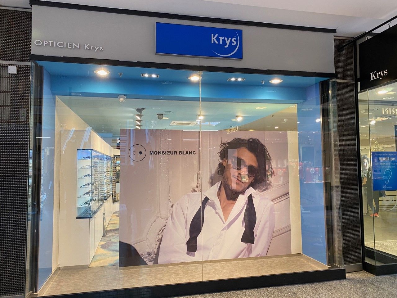 Vitrine ornée d'une grande affiche représentant une personne souriante en chemise blanche et cravate noire sous une enseigne bleue.