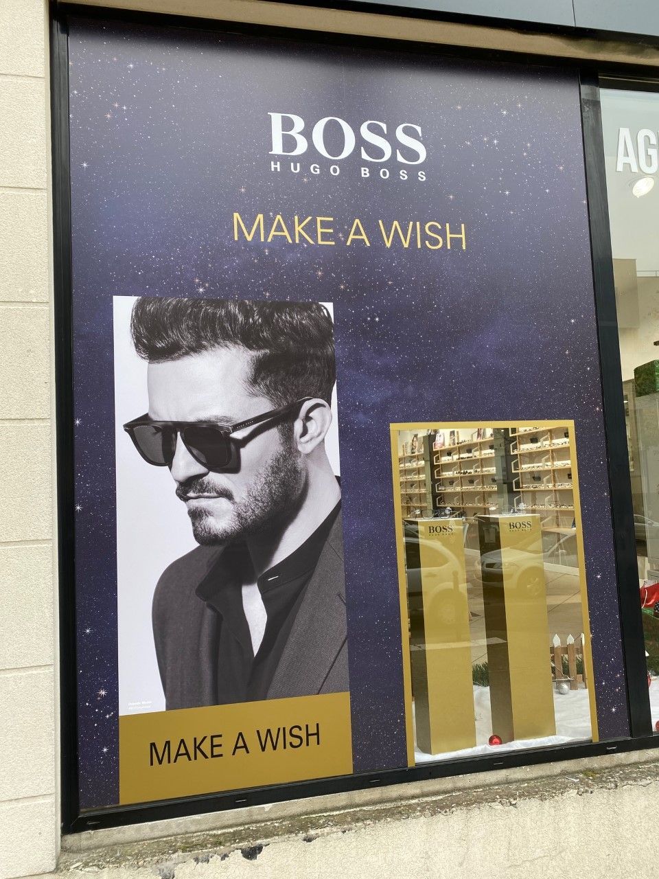Publicité en vitrine pour Hugo Boss avec mannequin en noir et blanc, inscription dorée FAITES UN SOUHAIT et présentoir de parfum