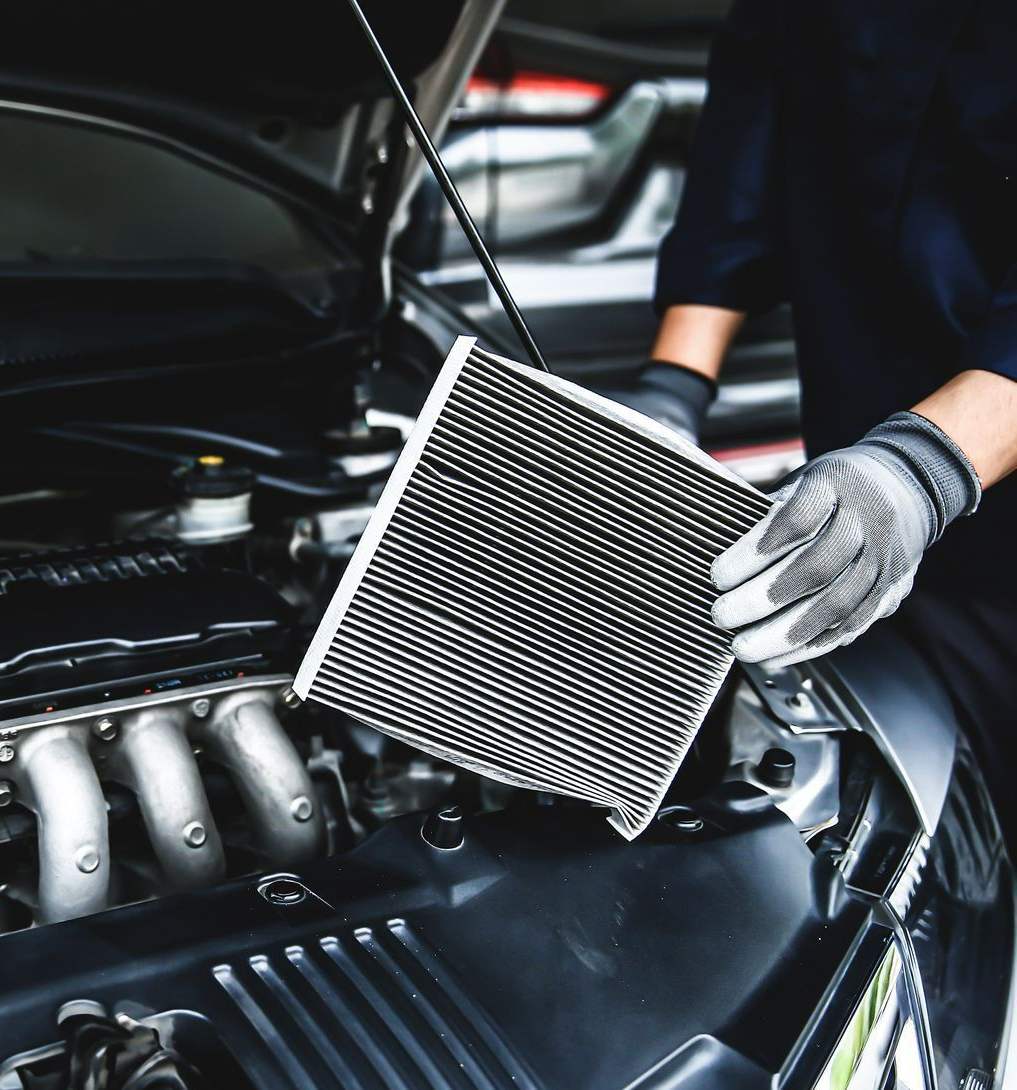 Un mécanicien tient un filtre à air neuf près d'un moteur de voiture ouvert.