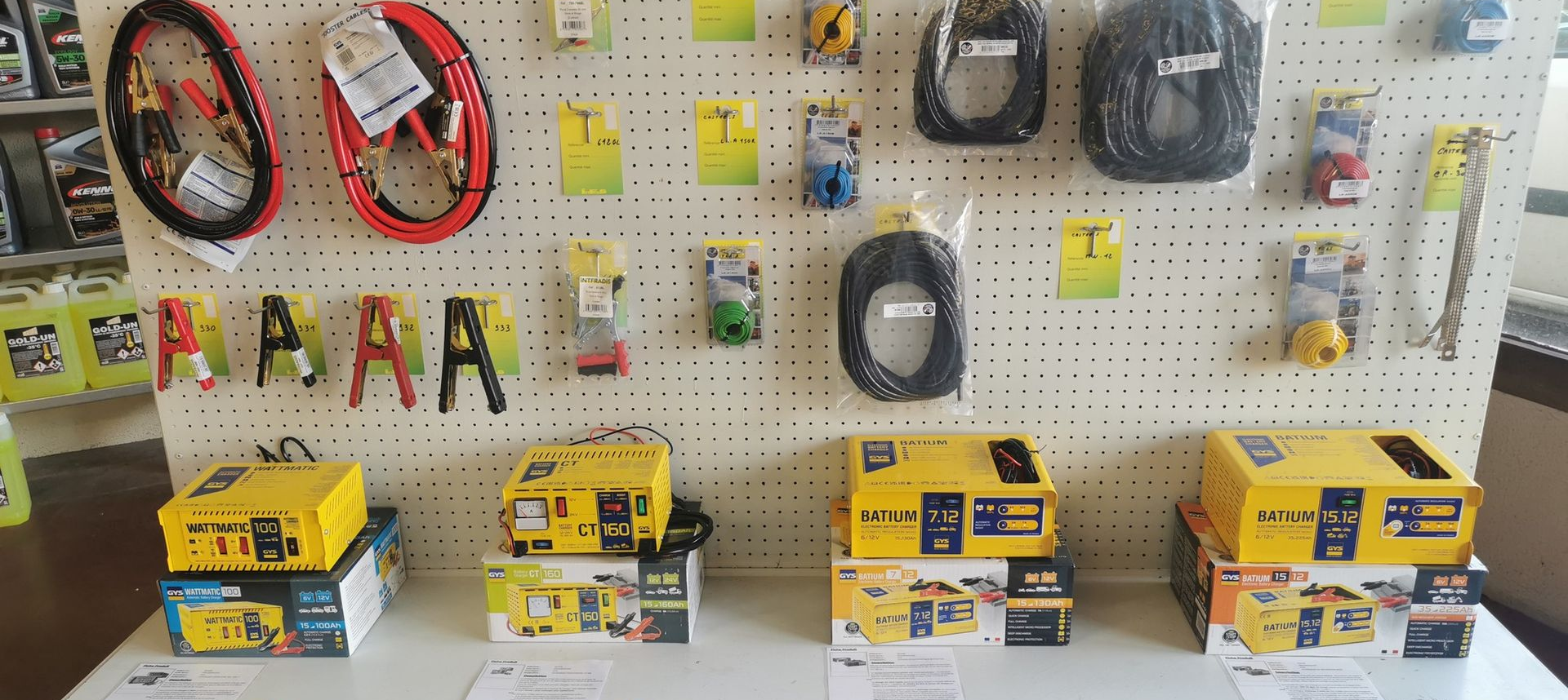 Présentation d'accessoires automobiles sur un panneau perforé : câbles de démarrage, pinces, chargeurs et rallonges.