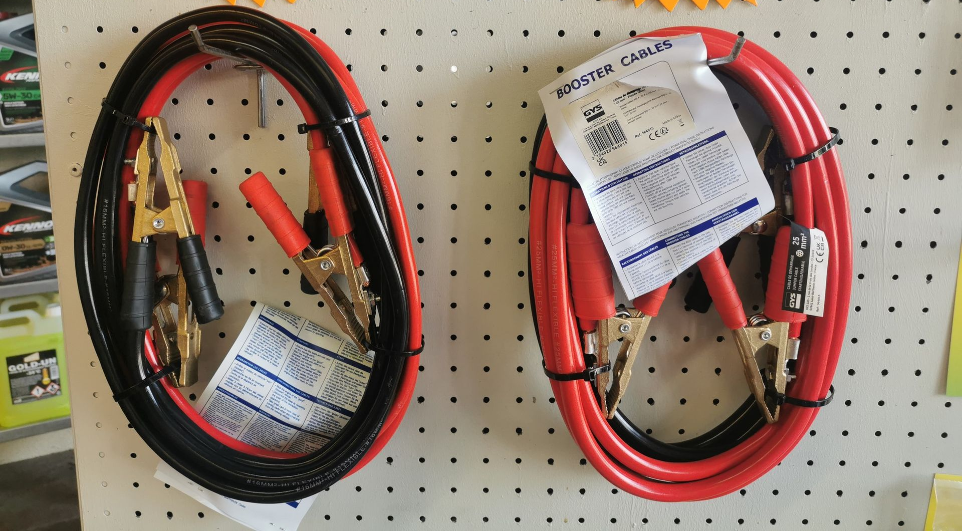 Deux jeux de câbles de démarrage enroulés, rouges et noirs, avec leurs étiquettes de prix, accrochés au mur.