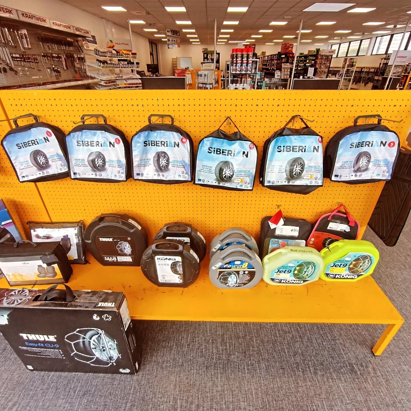 Présentation de chaînes à neige et d'accessoires dans un magasin, notamment des sacs de chaînes.
