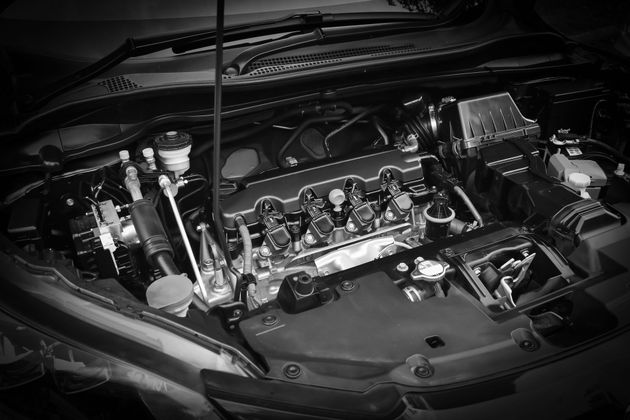 Gros plan en noir et blanc d'un moteur de voiture, capot ouvert, montrant divers composants mécaniques.