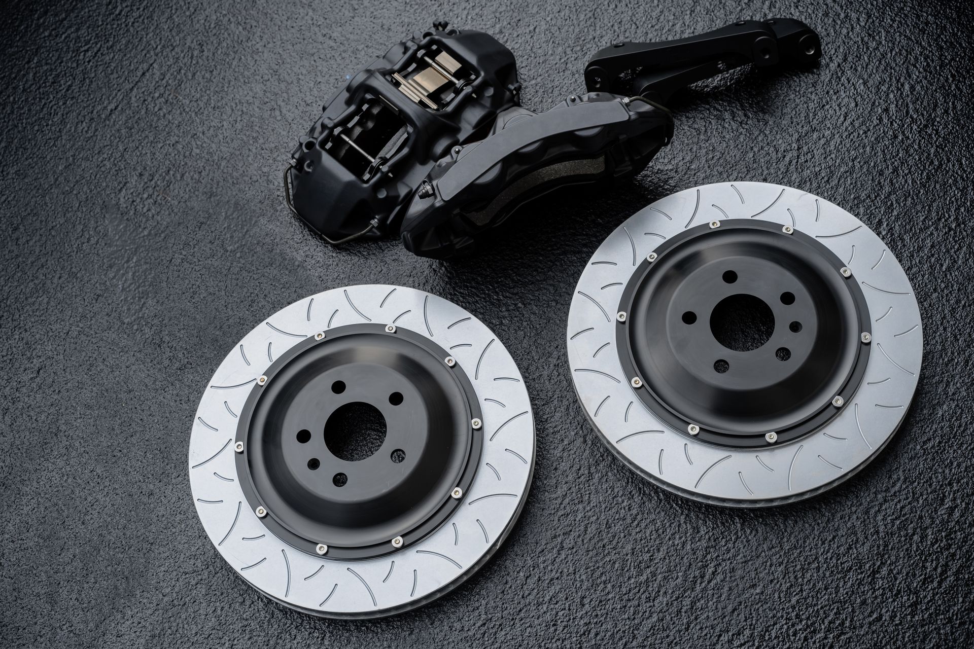 Deux disques de frein rainurés et des étriers noirs sur une surface sombre texturée.