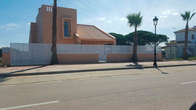 Una casa con una cerca blanca y palmeras al costado de la carretera.