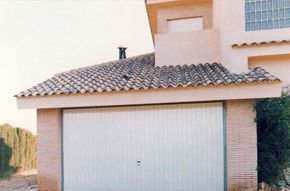 Una puerta de garaje blanca está delante de una casa con techo de tejas.