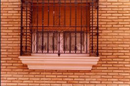 Una pared de ladrillos con una ventana con una valla de hierro forjado alrededor.