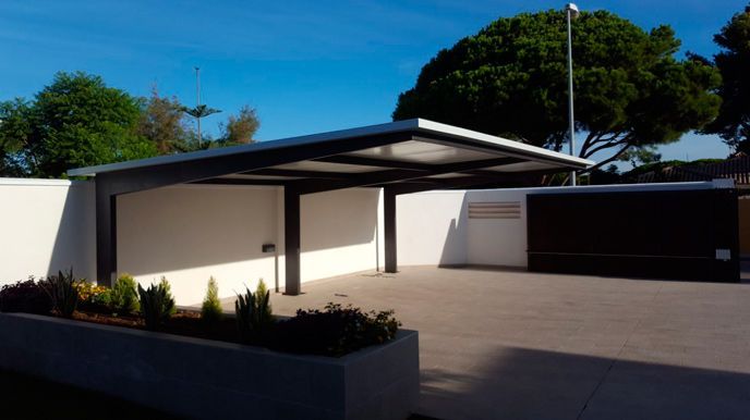 Una cochera frente a una casa con árboles al fondo.