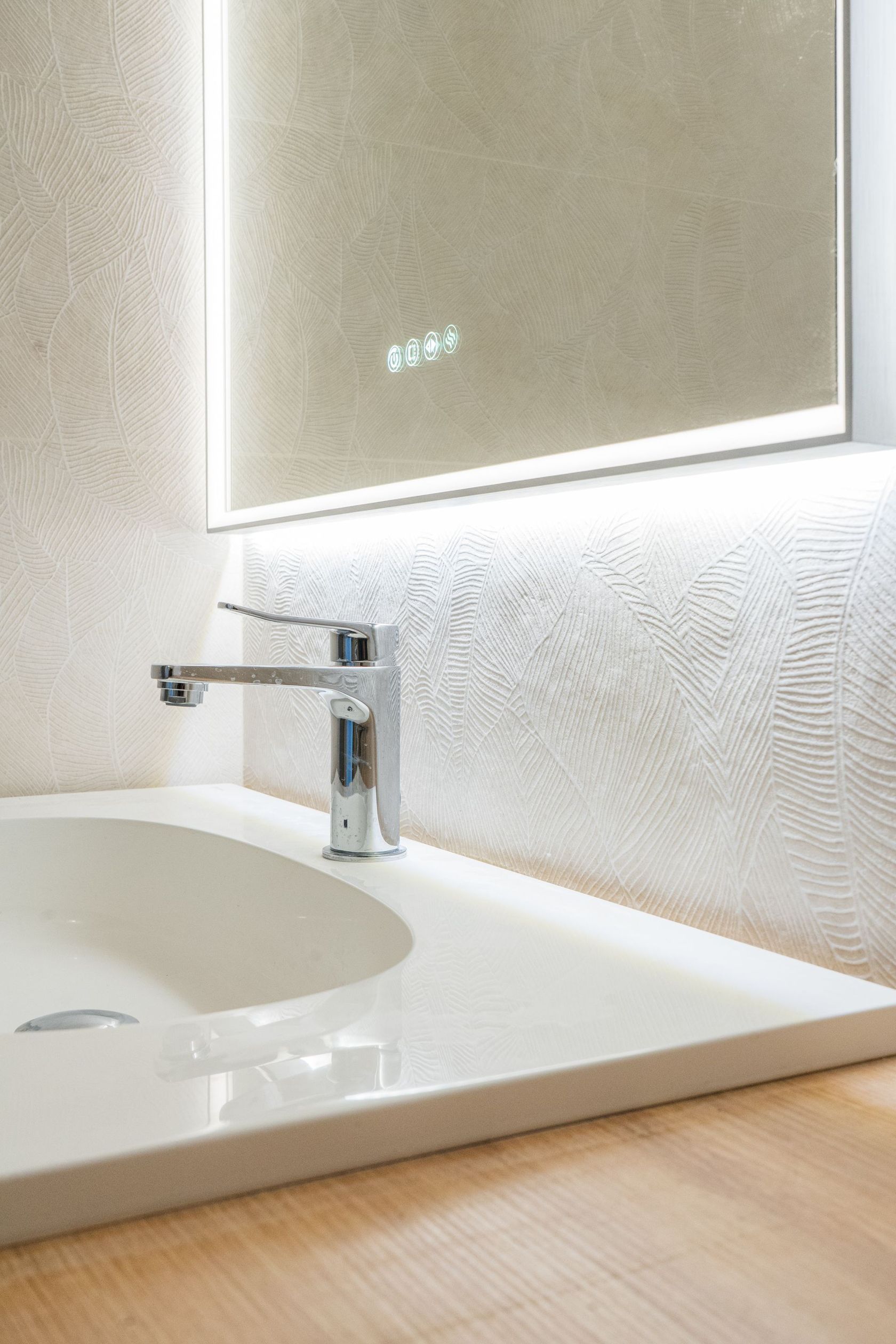 Lavabo blanc avec robinet chromé, miroir éclairé au dessus, mur texturé.