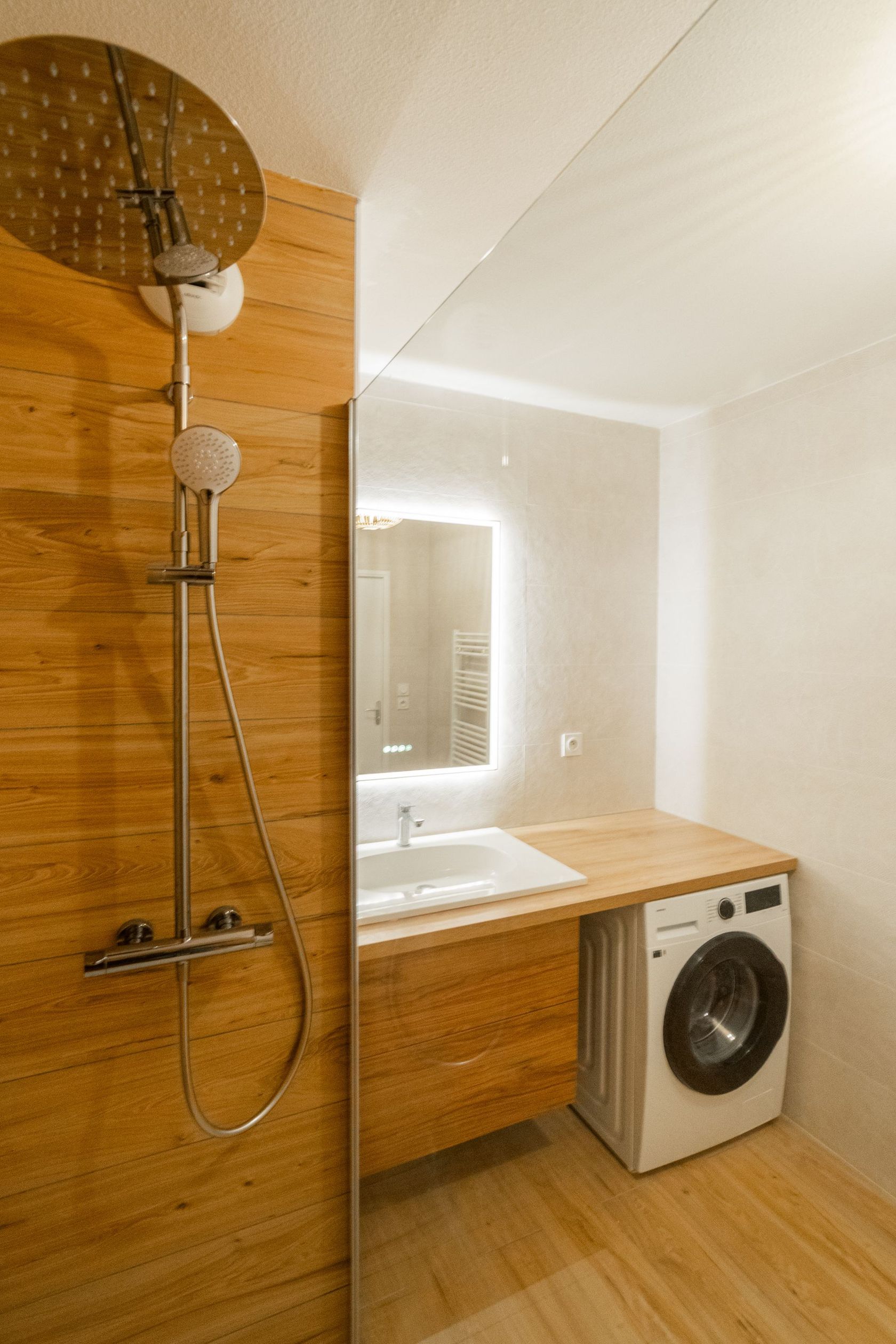 Salle de bain moderne avec boiseries, douche à effet pluie et lave-linge.