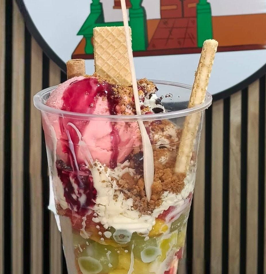 Vaso alto de postre de frutas colorido con helado, crema batida, barquillos y sirope de chocolate.