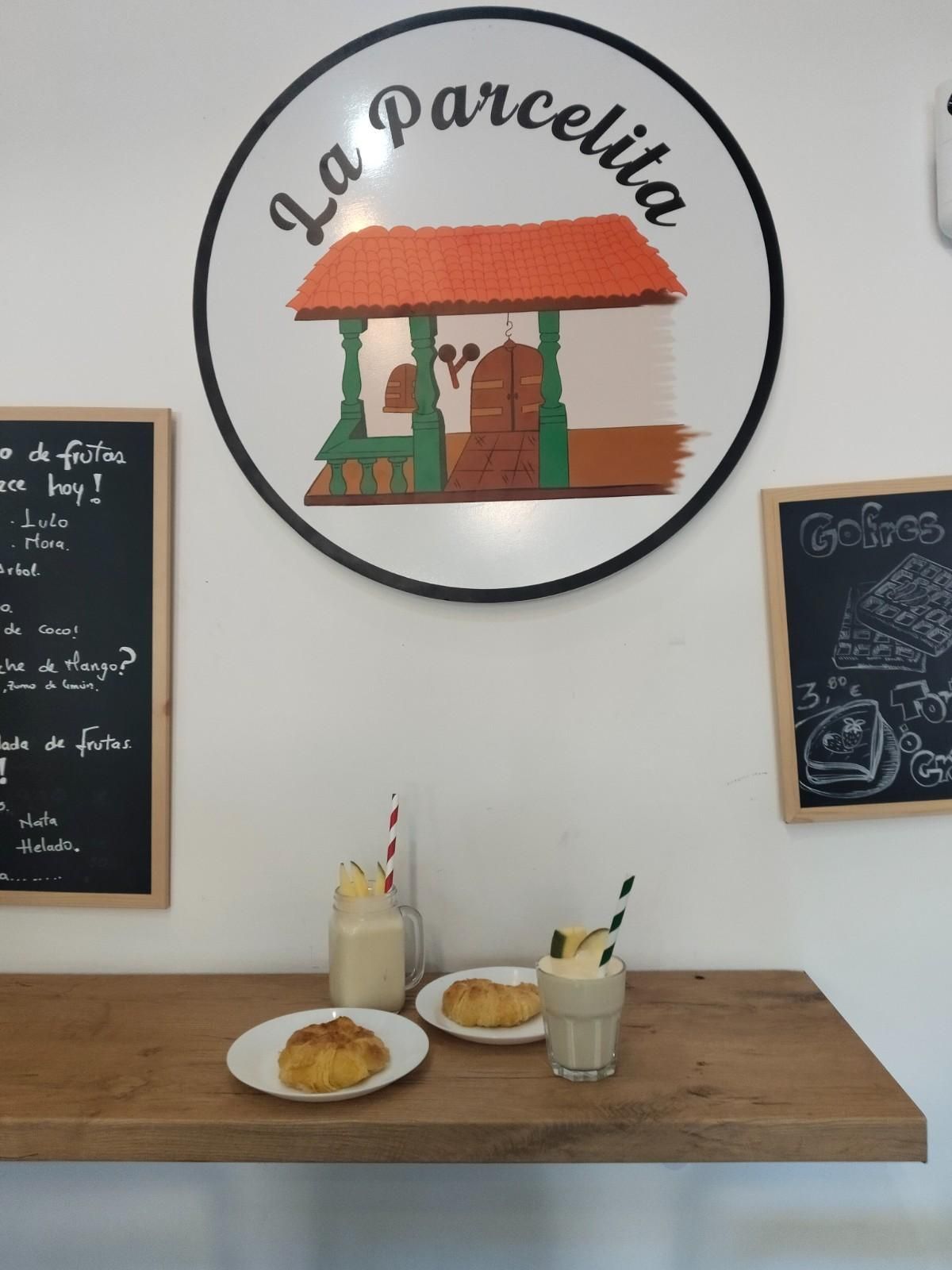Pequeña barra de cafetería con pasteles, bebidas y un letrero redondo de “La parcería” en la pared.