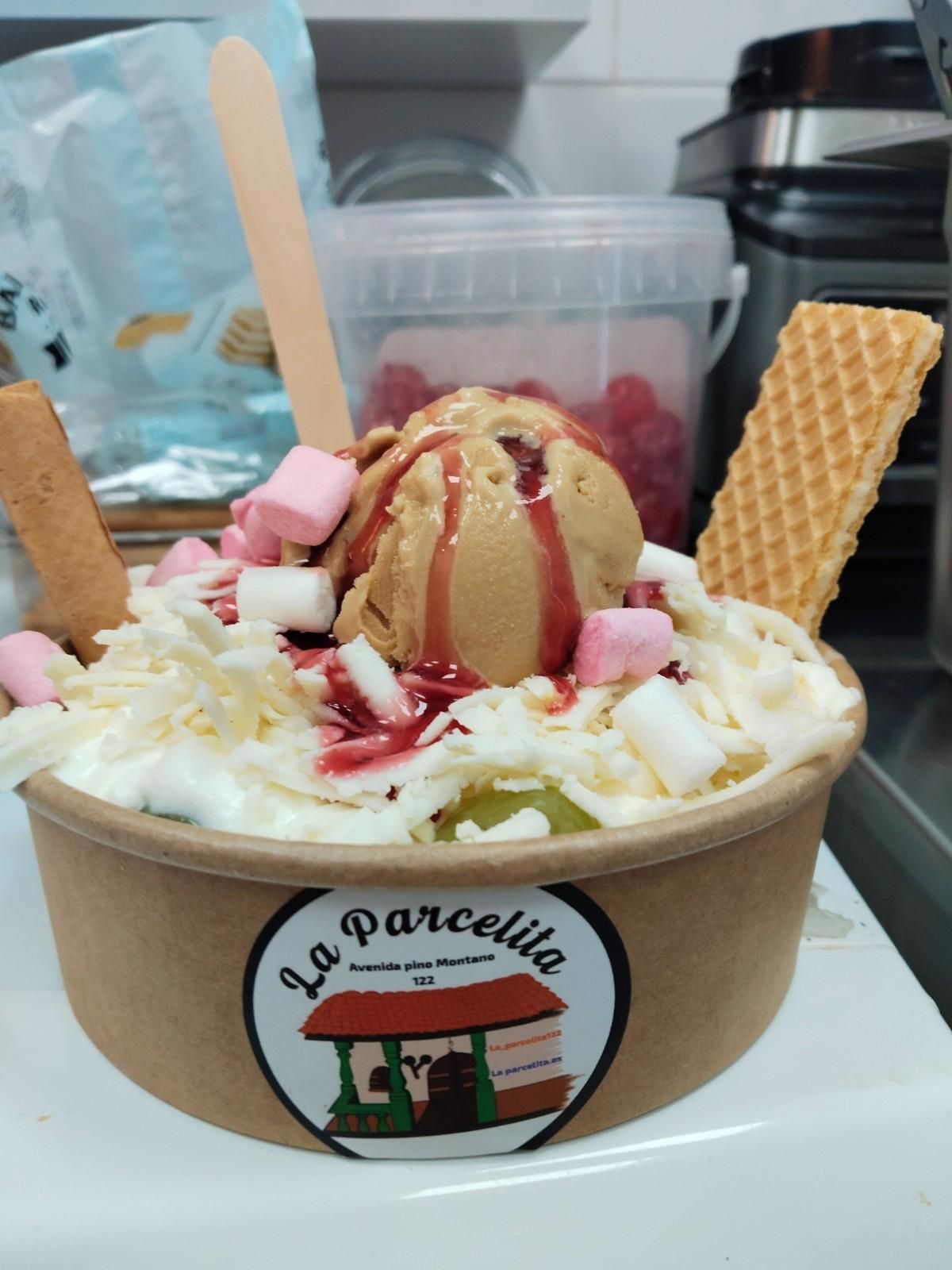 Sundae de helado en un vaso de cartón con barquillos, crema batida, malvaviscos y sirope de frutos rojos.