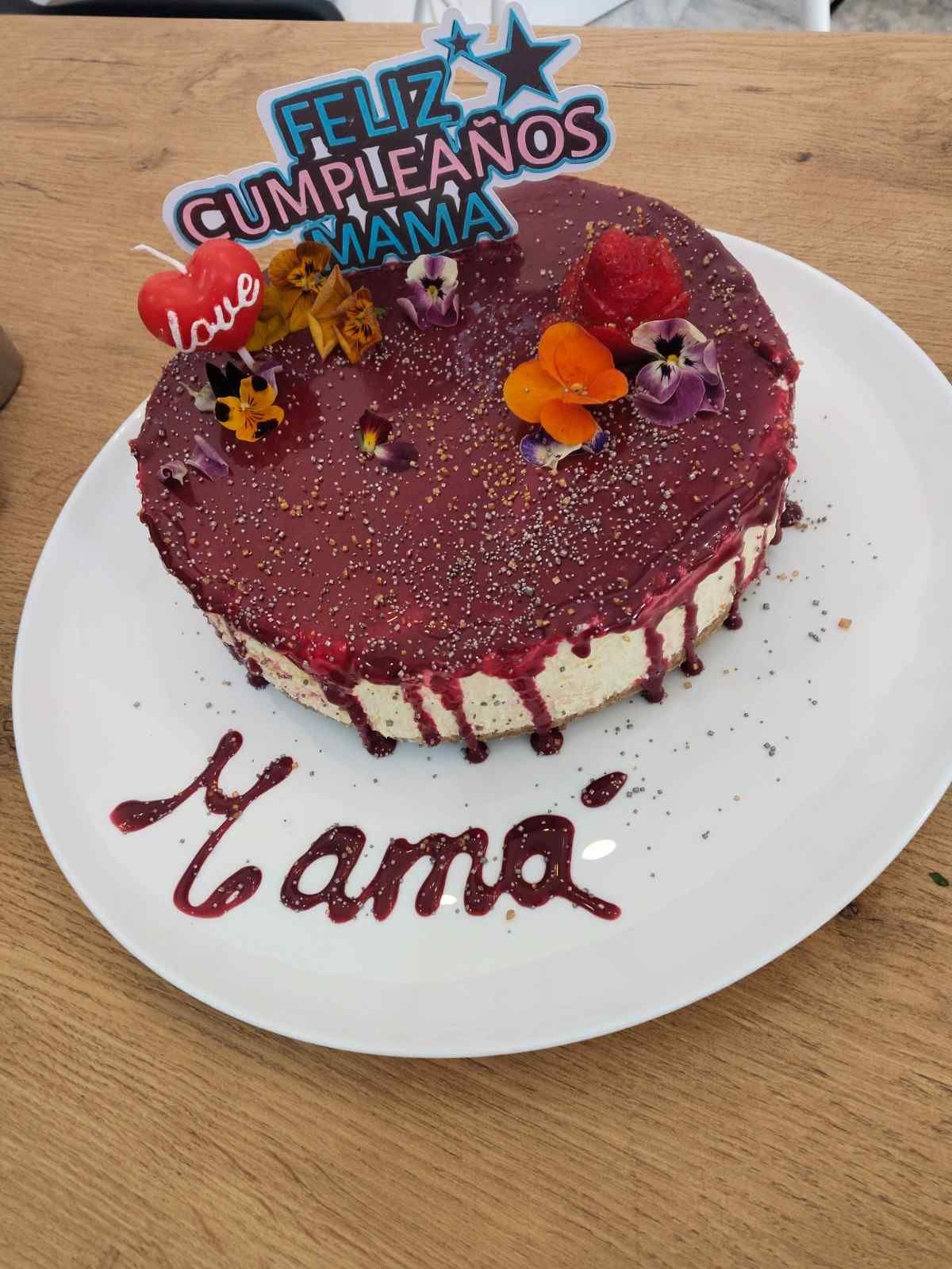 Maroon birthday cake with flowers and “Feliz cumpleaños mamá” topper on a white plate labeled “Mamá”.