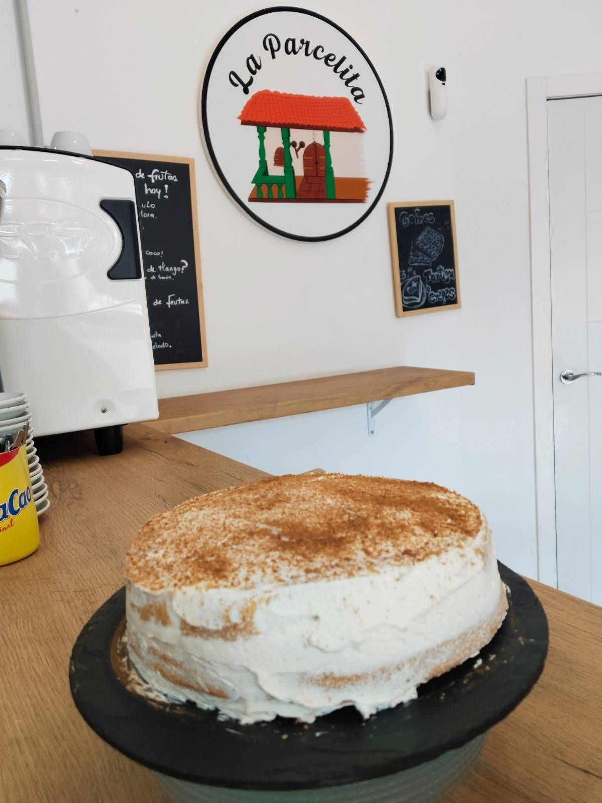 Pastel redondo glaseado sobre una bandeja negra en la cocina de una cafetería, espolvoreado con canela o cacao.