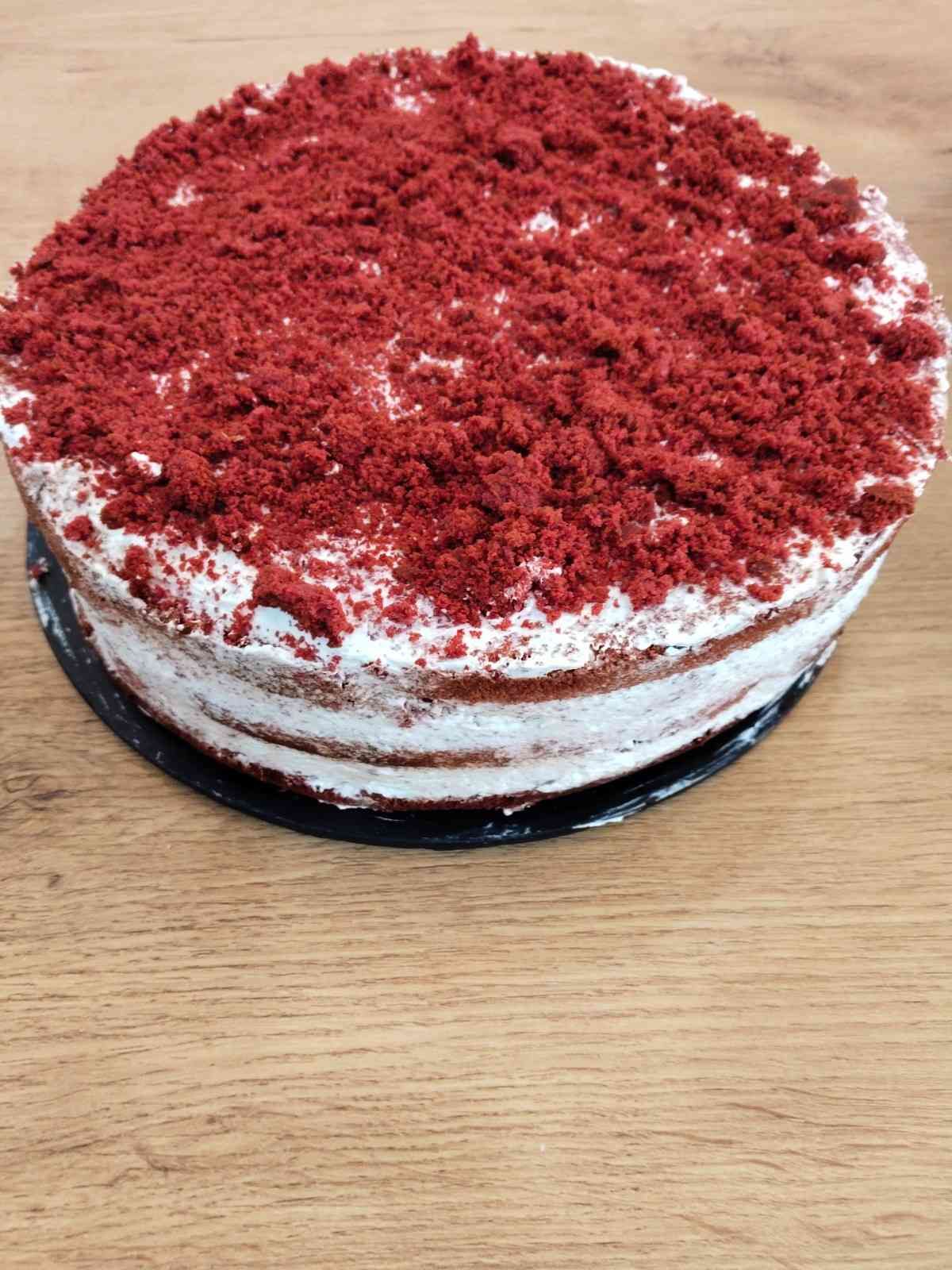 Tarta de terciopelo rojo con glaseado blanco sobre una base negra para tartas, colocada sobre una mesa de madera.