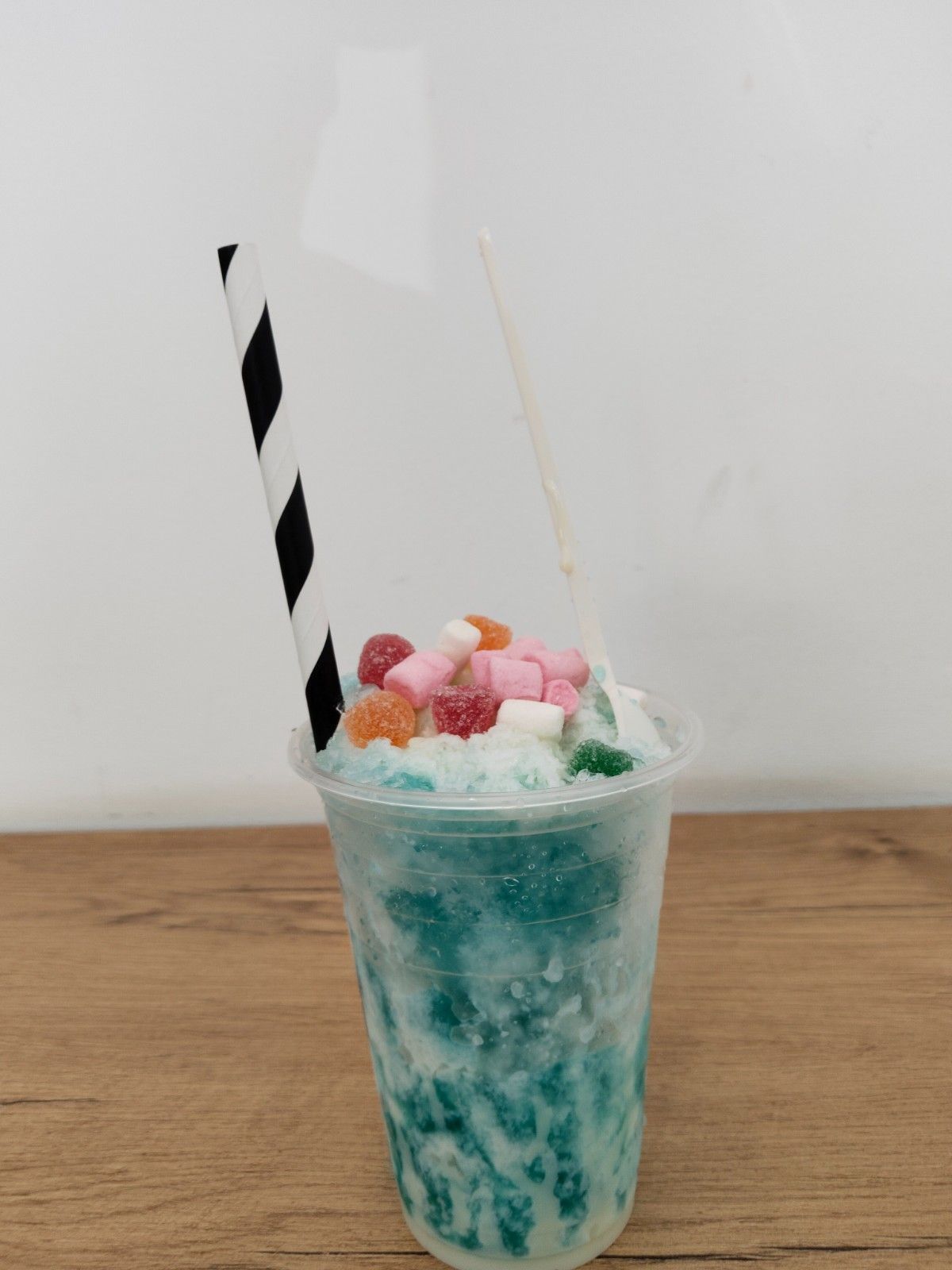 Bebida granizada azul con crema batida, malvaviscos de colores y una pajita a rayas en un vaso transparente.