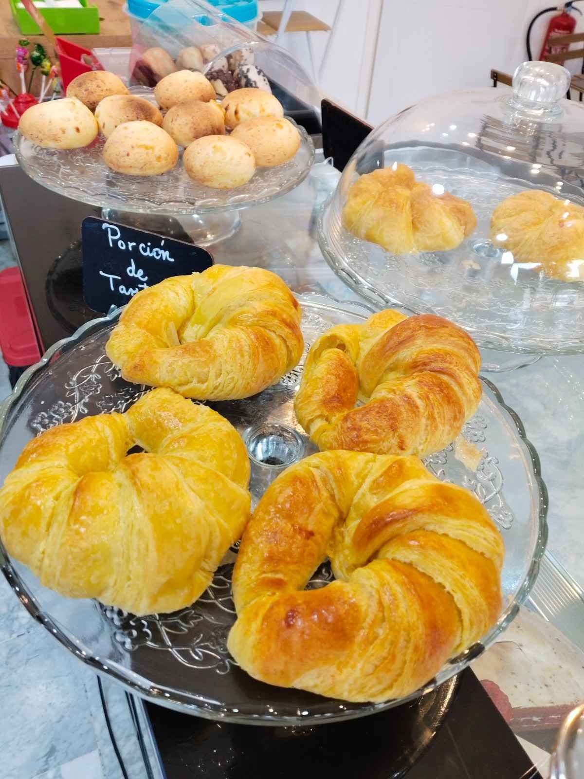 Surtido de croissants y pasteles dorados en una bandeja de cristal en el mostrador de una panadería.