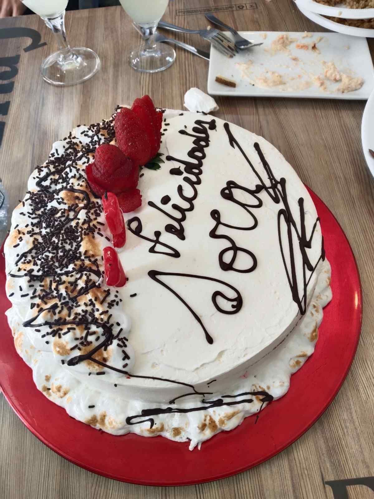 Tarta de cumpleaños blanca con frambuesas, sirope de chocolate y la inscripción 