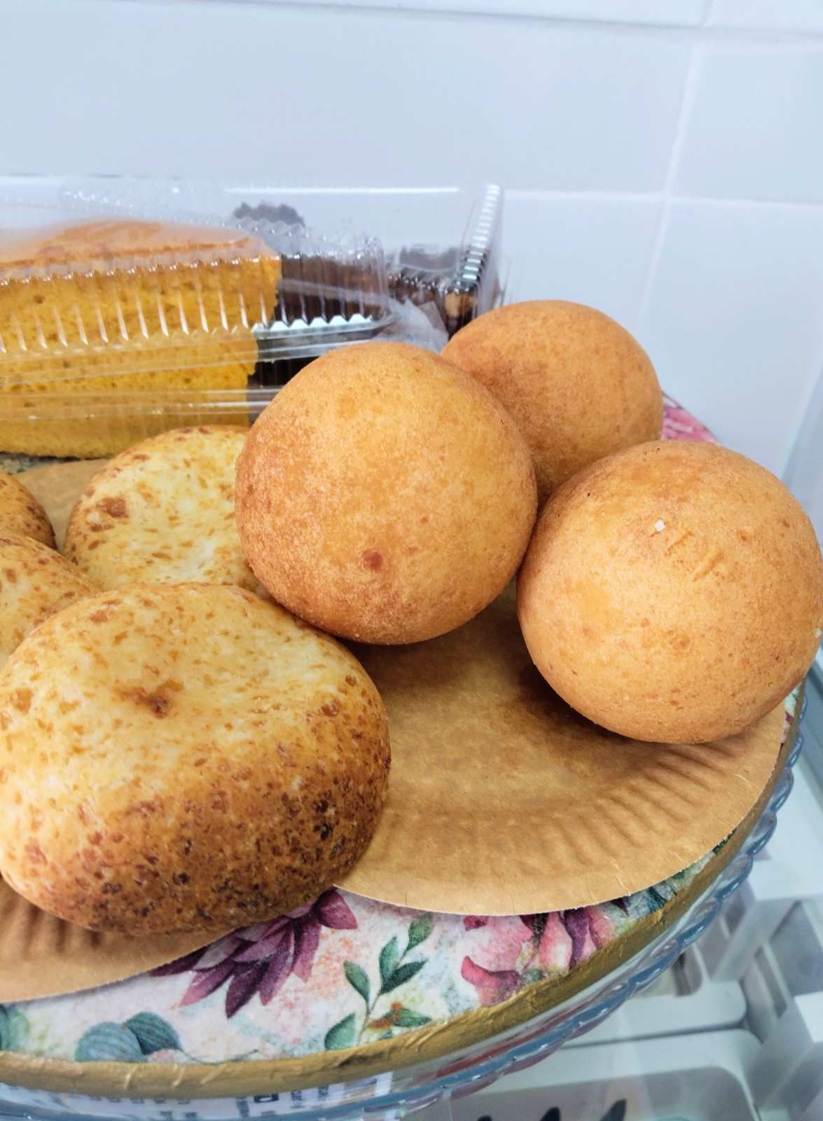 Variedad de panecillos redondos y rebanadas de pan en un plato floral en una cocina.