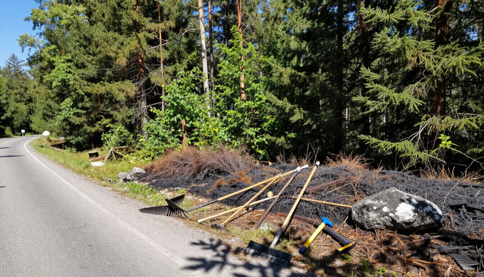 En un día soleado, unas herramientas reposan al borde de la carretera, cerca de una zona de vegetación quemada.