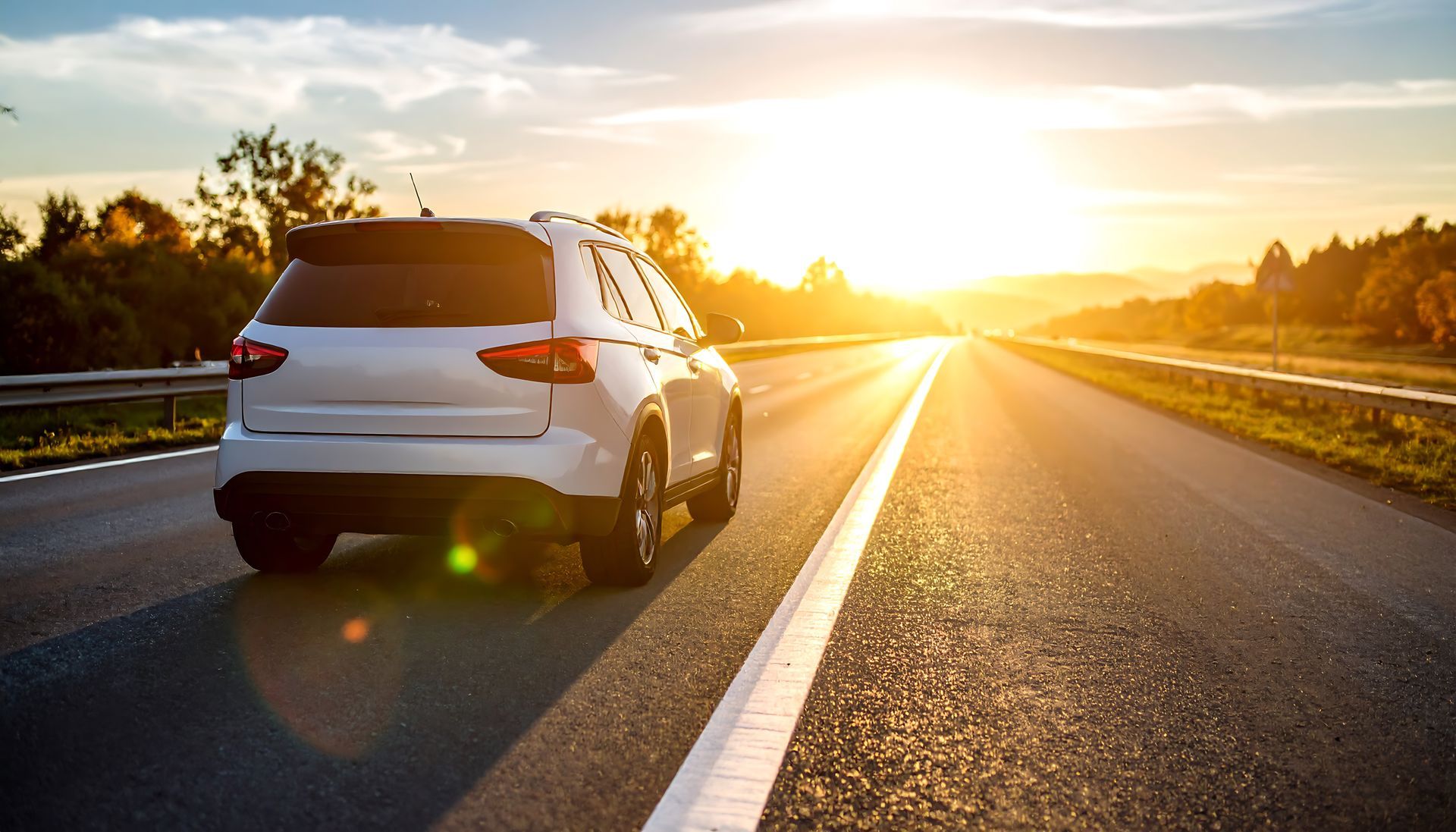 SUV blanc roulant sur une autoroute ouverte au coucher du soleil.