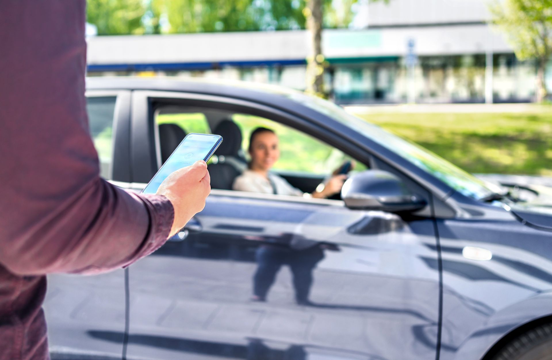 Une personne tenant une tablette à côté d'une voiture, le conducteur regardant devant lui dans un environnement de jour.