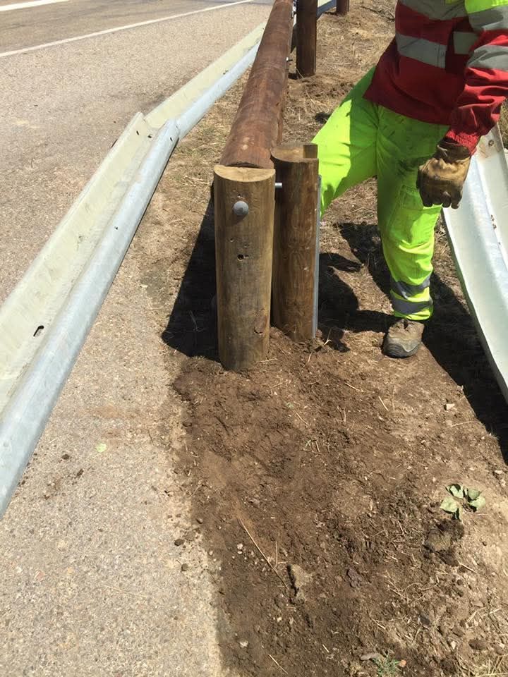 Un hombre está de pie junto a una valla de madera al costado de la carretera.