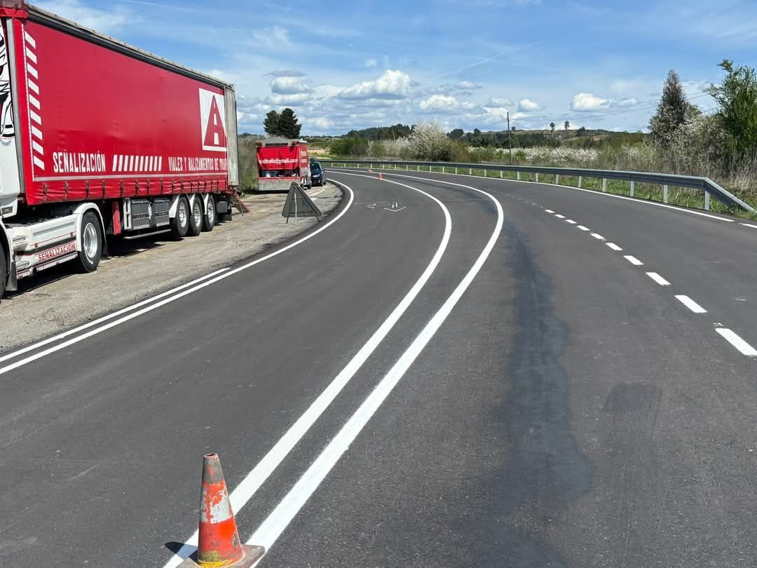 Un camión semirremolque rojo está estacionado al costado de una carretera con curvas.