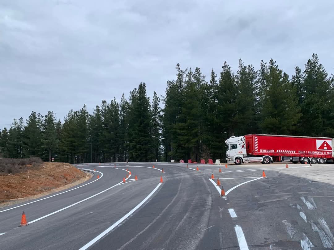 Un camión circula por una carretera con curvas al lado de un bosque.
