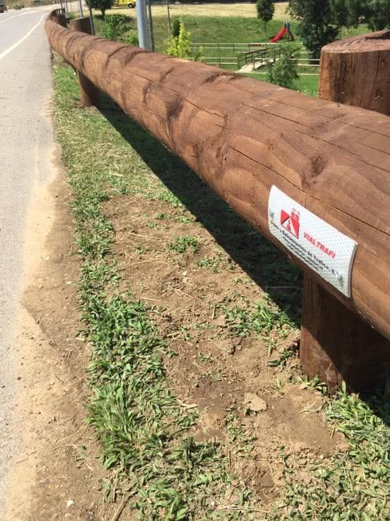 Una valla de madera con una pegatina está al lado de una carretera.